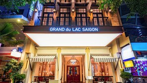 The exterior of the GRAND du LAC SAIGON hotel, featuring a prominent entrance with a grand archway, multiple balconies, and lush greenery surrounding the building. - GRAND HOTEL du LAC Boutique Saigon (Ho Chi Minh City)