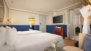 A hotel room with two beds, a TV, a minibar, and a bathroom visible through a glass door.