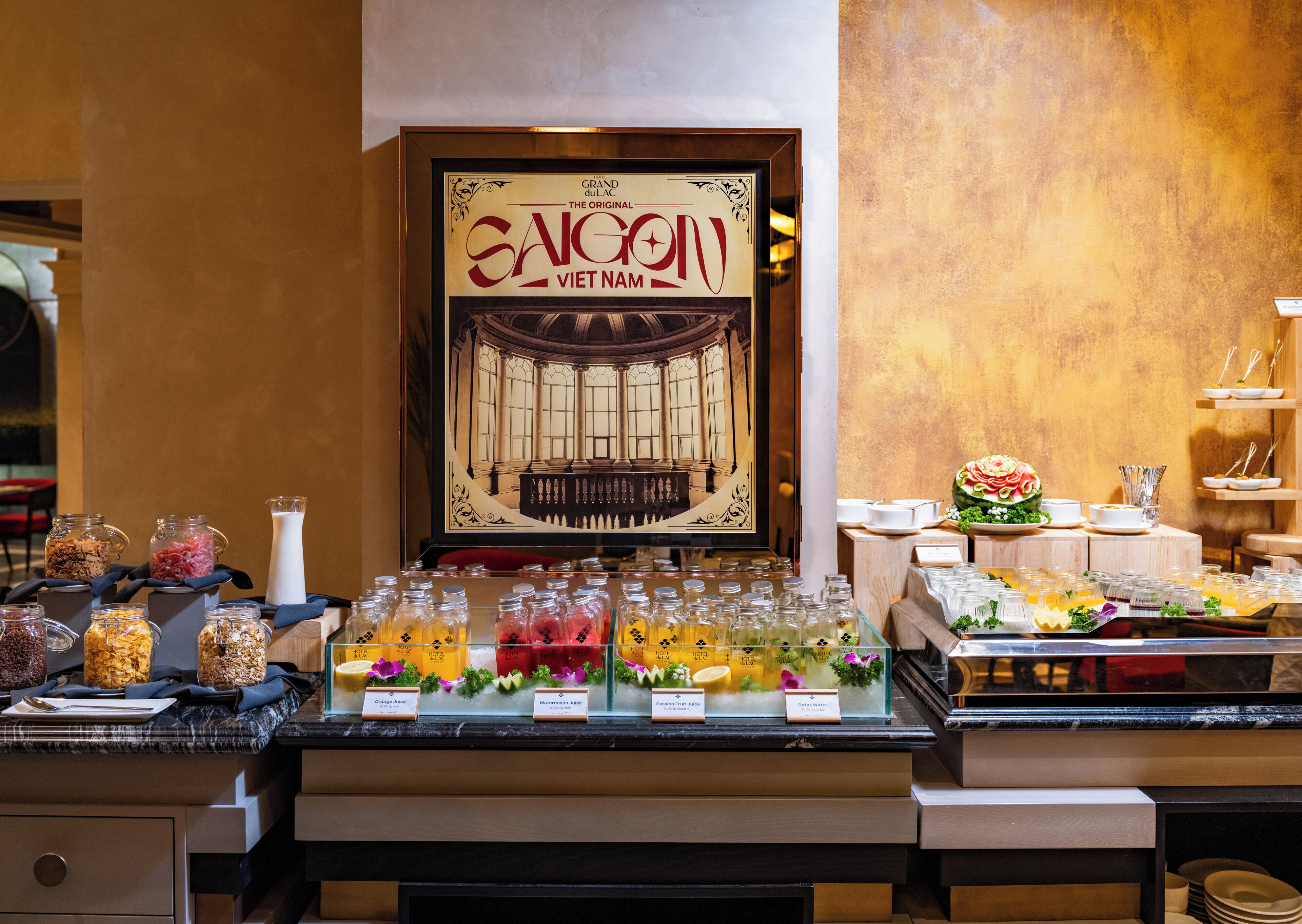 A buffet area with various food items and beverages, including jars of fruits and juices, and a framed menu titled "SANG" in the background.