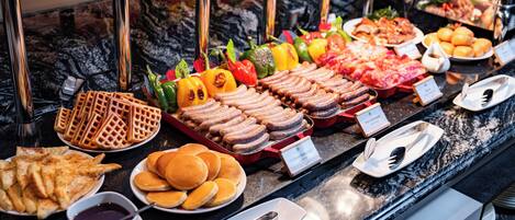 A buffet with various food items including waffles, pancakes, sausages, and vegetables.