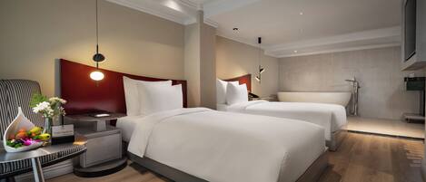 Quarto de hotel moderno com duas camas, uma escrivaninha, uma cadeira, mesa de cabeceira, um vaso com flores e uma televisão.