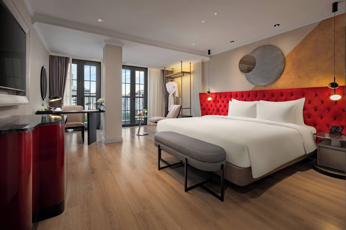 A modern hotel room with a large bed, a desk, and a seating area.