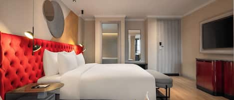 Une chambre d’hôtel moderne avec un grand lit, une tête de lit rouge en tissu, un téléviseur à écran plat et un panier de fruits sur la table de chevet.