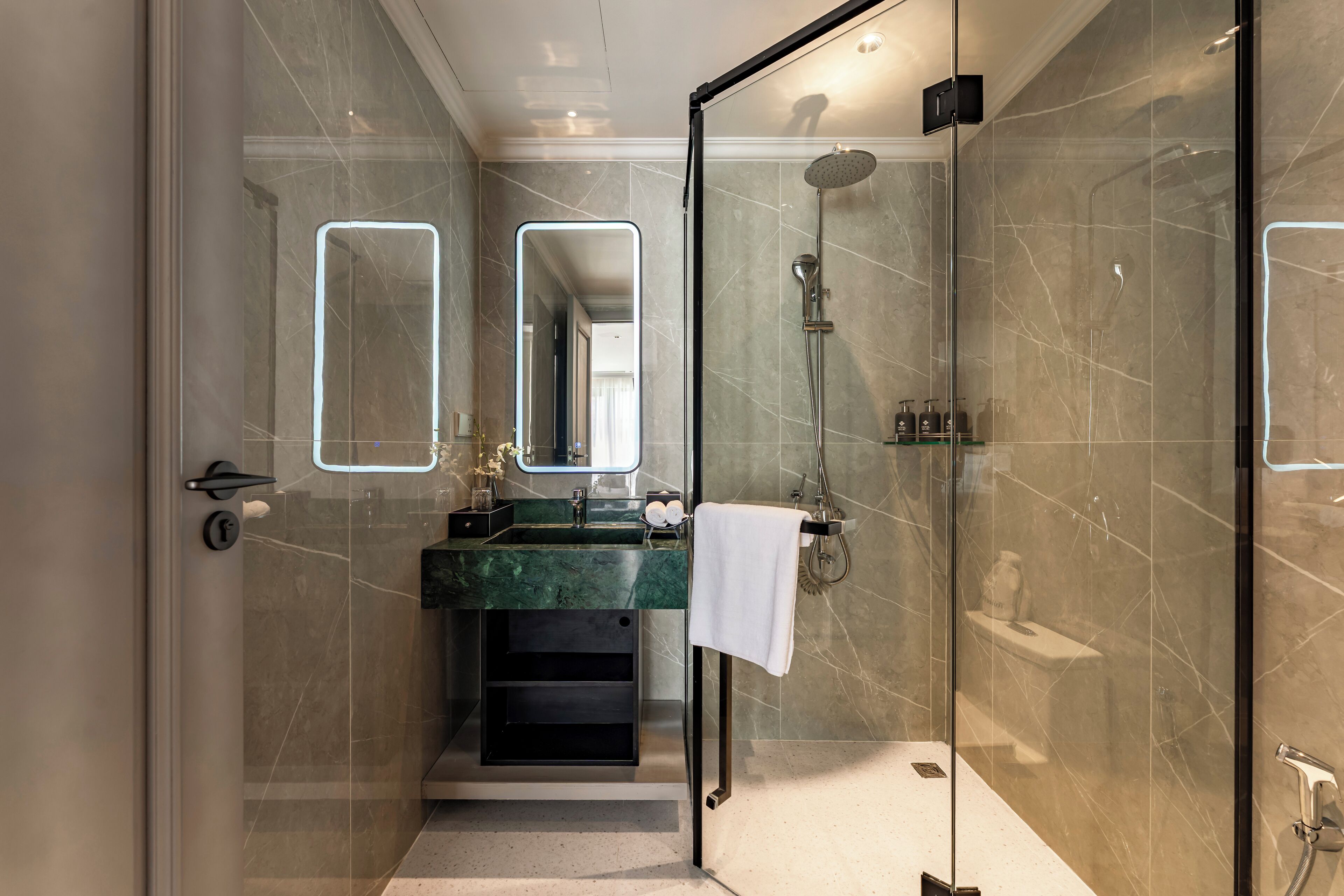 Un baño moderno con ducha de vidrio, lavamanos de mármol y un espejo grande.