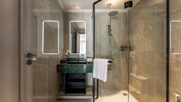 Un baño moderno con ducha de vidrio, lavamanos de mármol y un espejo grande.