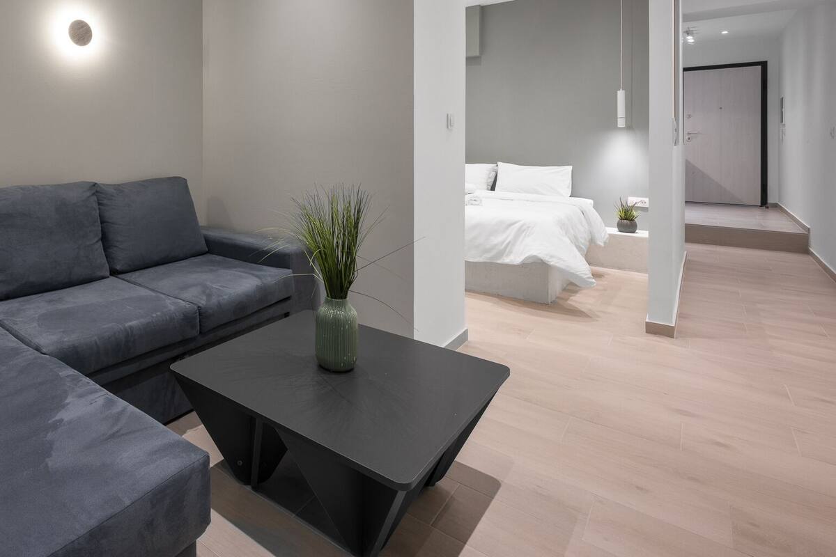 Ein modernes Wohnzimmer mit einem grauen Ecksofa, einem schwarzen Couchtisch und einer kleinen grünen Pflanze.