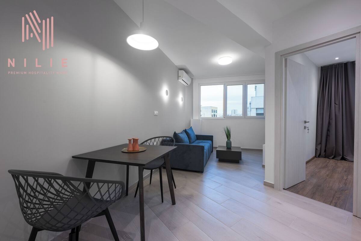 Ein modernes Wohnzimmer mit Essbereich, einer Couch und einem kleinen Tisch mit Stühlen. Ein Fenster bietet Blick auf Gebäude.