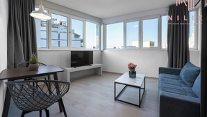 A modern living room with a sofa, a dining table with chairs, a TV, and a coffee table. - Venus, Nilie Hospitality MGMT (Thessaloniki)