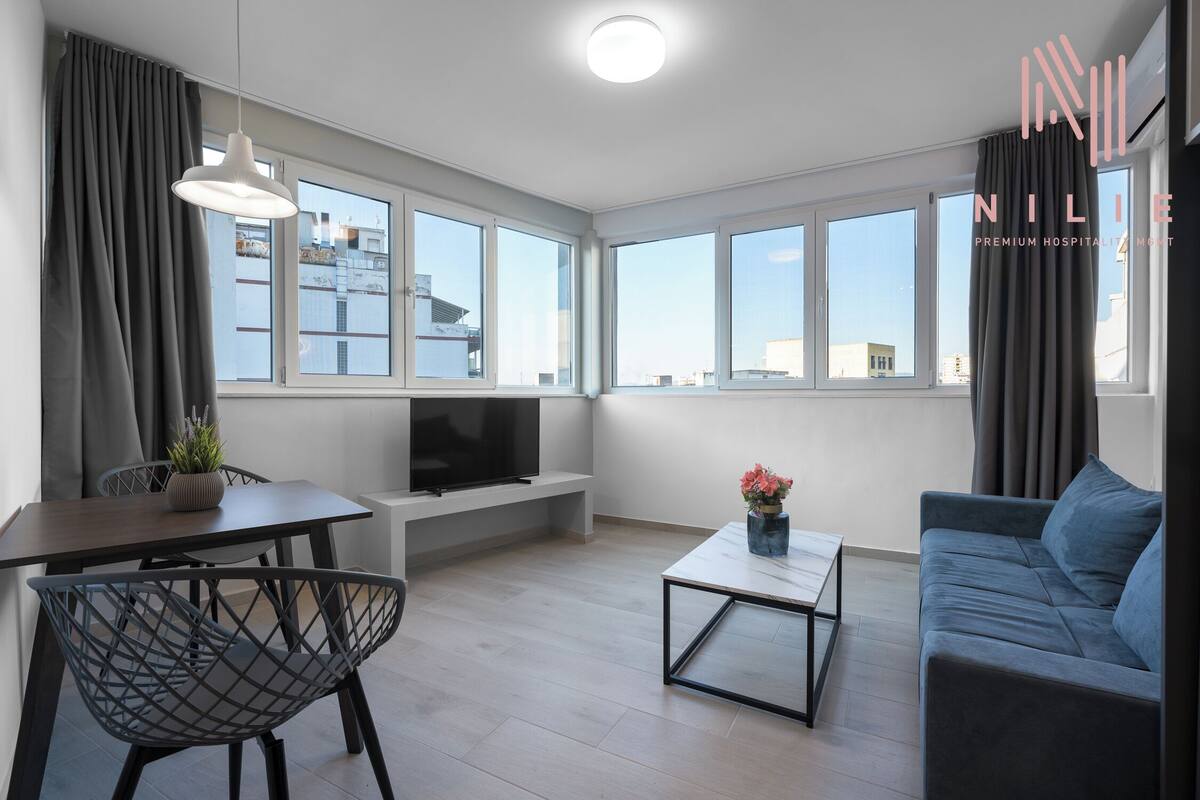 Ein modernes Wohnzimmer mit Sofa, Esstisch mit Stühlen, Fernseher und Couchtisch.