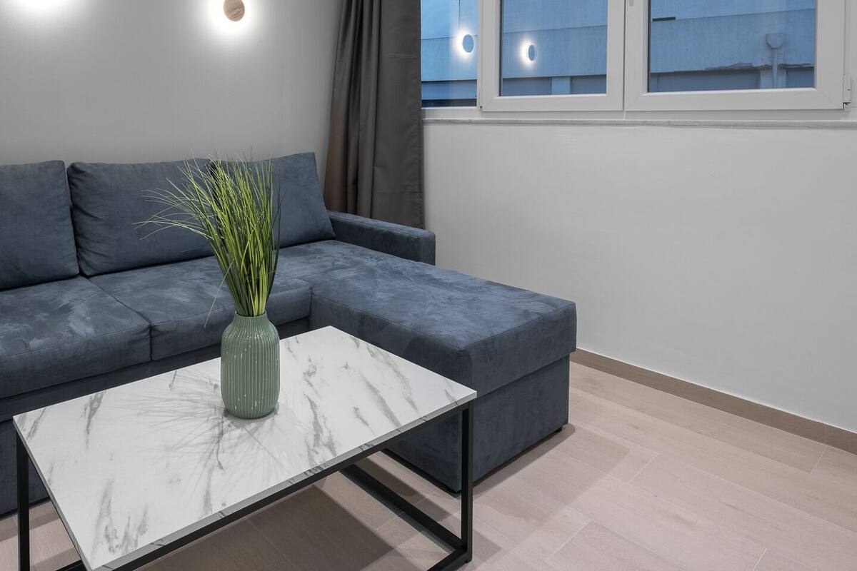 Ein modernes Wohnzimmer mit einem grauen Sofa, einem weißen Marmor-Couchtisch und einer grünen Vase mit Pflanzen.