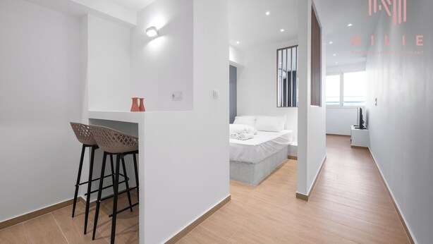 A modern, minimalist bedroom with a large bed, a small desk with two chairs, and a bright window. - Venus, Nilie Hospitality MGMT (Thessaloniki)