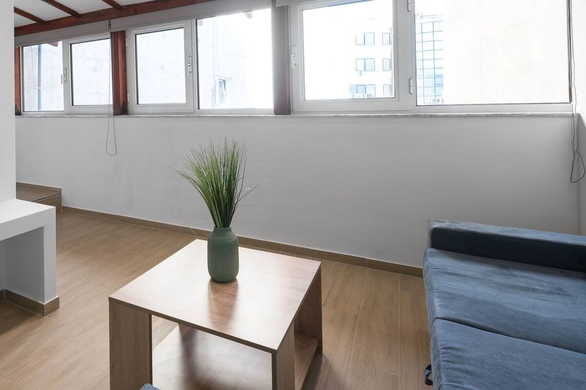 Ein modernes Wohnzimmer mit Flachbildfernseher, blauem Sofa, Couchtisch aus Holz und einer Topfpflanze.