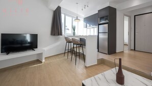 A modern kitchen with a built-in oven and microwave, a dining area with a bar stool, and a flat-screen TV mounted on a white console. - Venus, Nilie Hospitality MGMT (Thessaloniki)