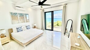 Een moderne slaapkamer met een groot bed, een plafondventilator en uitzicht op de oceaan door een schuifdeur van glas.