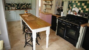 A kitchen with a wooden table, stools, a stove, and various kitchen appliances. - House Sleeps 9-garden-pool-bbq-patio-parking (Maidstone)