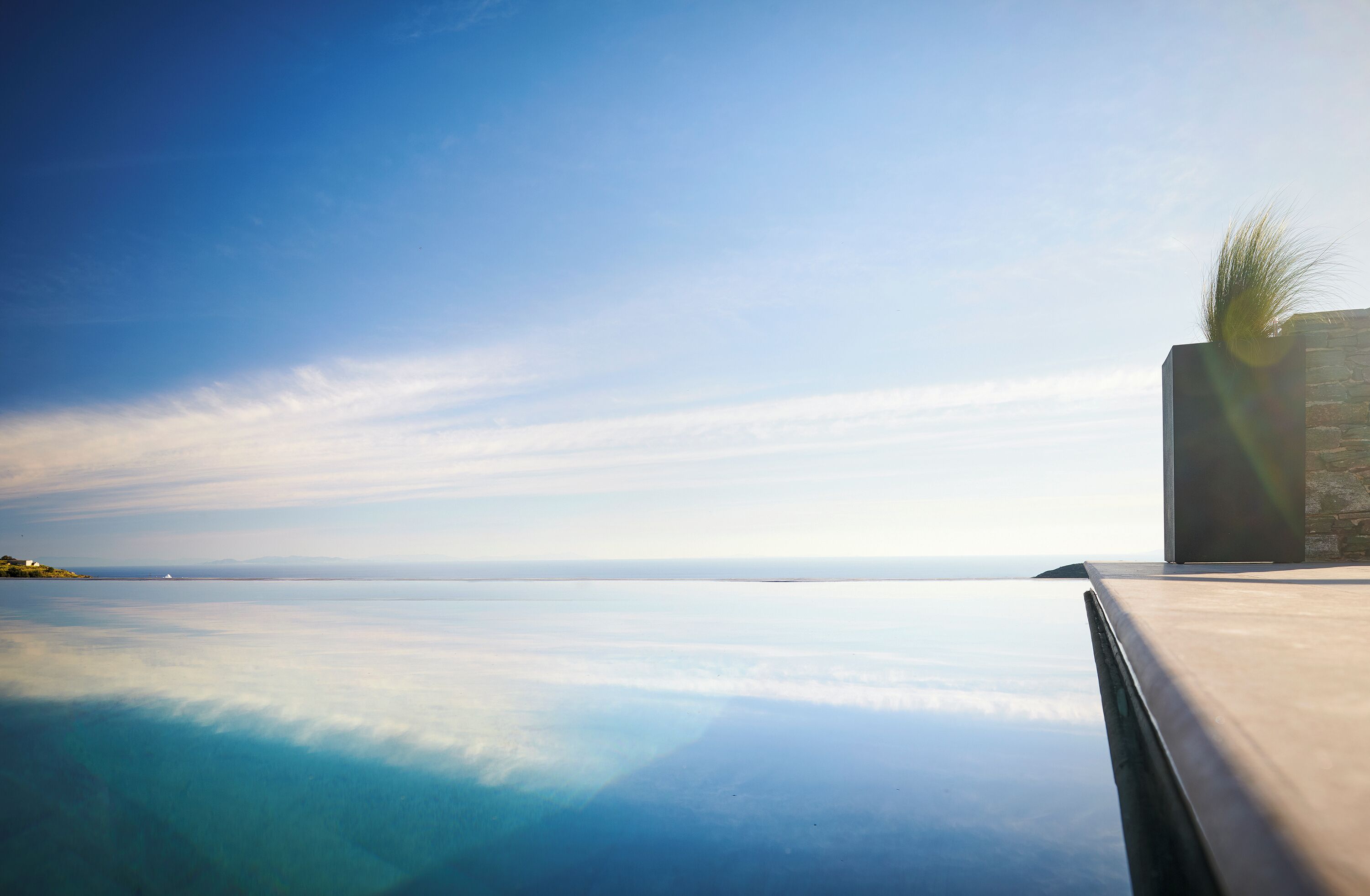 A clear view of an infinity pool with a stone structure on the right and a clear blue sky above.