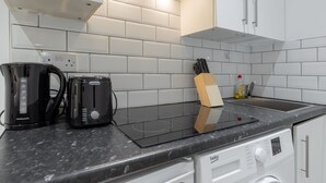A kitchen with white tiled backsplash, a black induction cooktop, a coffee maker, and a bread maker. - Trio of Lovely Studio Apartments in Shoreditch (London)
