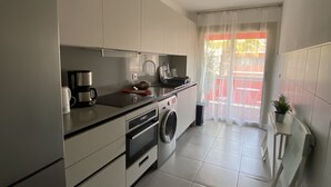 A modern kitchen with white cabinets, a coffee maker, a washing machine, and a small table with a plant. - Superb bright apartment, terraces free secure parking 600m from the sea (Cagnes-sur-Mer)