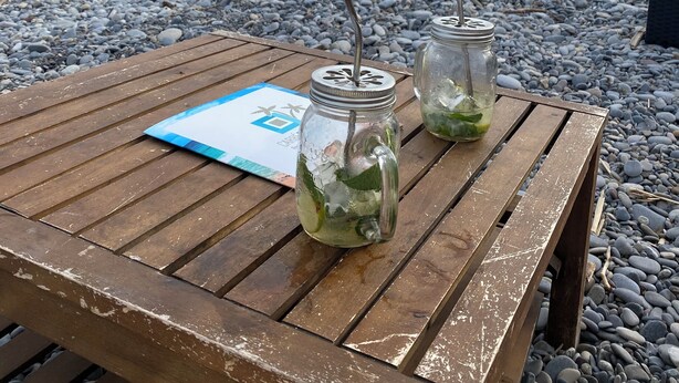 A wooden table with two mason jars containing a green drink, a menu, and a view of the beach and sea. - Superb bright apartment, terraces free secure parking 600m from the sea (Cagnes-sur-Mer)