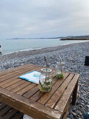 A wooden table with two mason jars containing a green drink, a menu, and a view of the beach and sea.