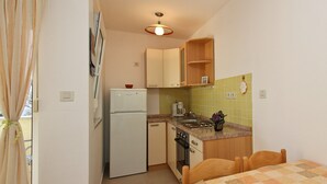 A compact kitchen with a refrigerator, stove, and sink. There is a dining table with chairs and a checkered tablecloth. - Charming studio Ljubica (Punat)