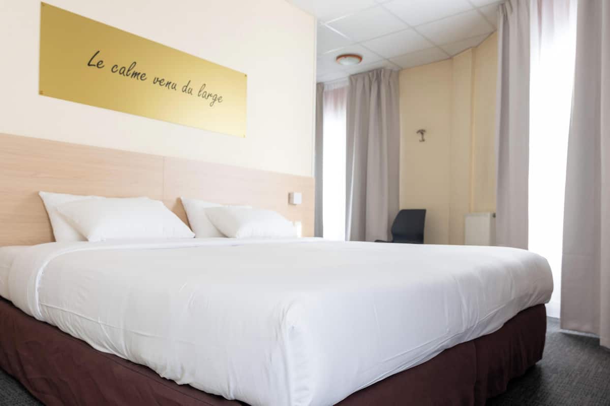 Camera d'albergo con un letto grande, una testiera, un comodino, una lampada e una finestra con tende.