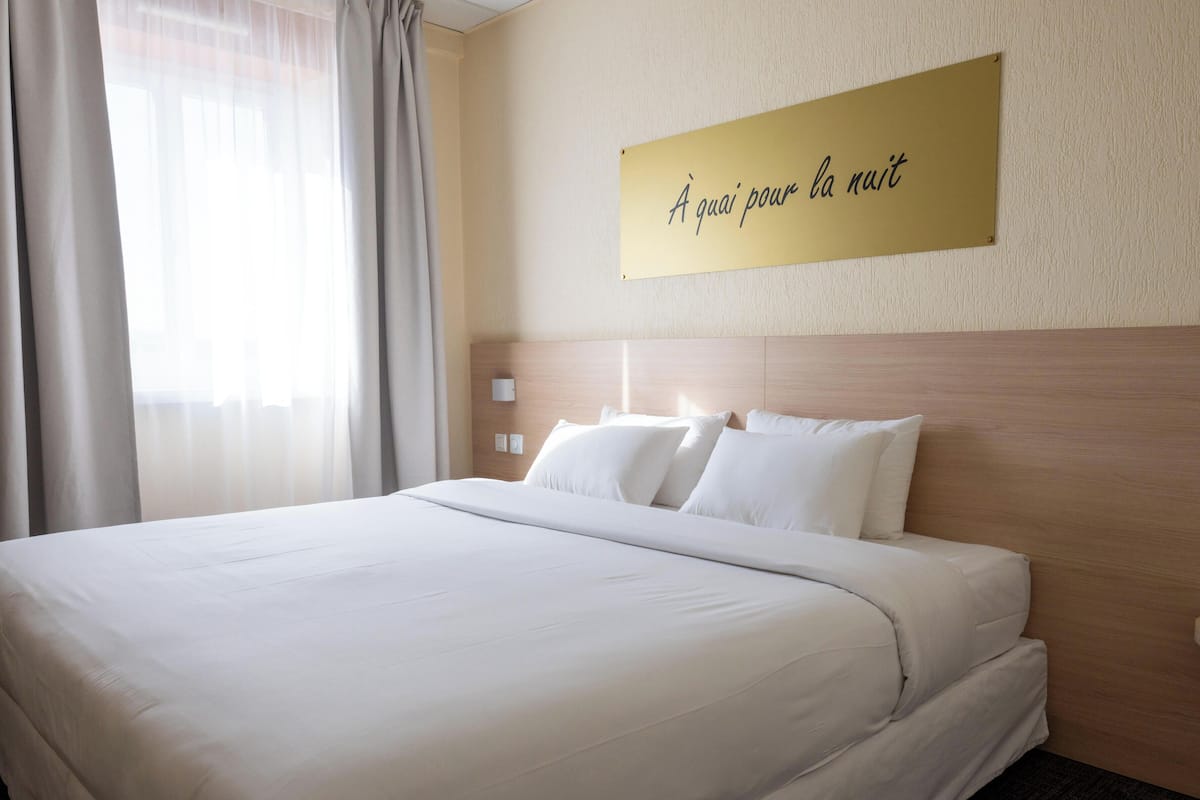 Una camera d'albergo con un letto grande, una testata, un comodino e un cartello appeso al muro.
