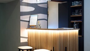 Eine moderne Bar mit Holztresen, zwei Hockstühlen und hängenden Pendelleuchten.