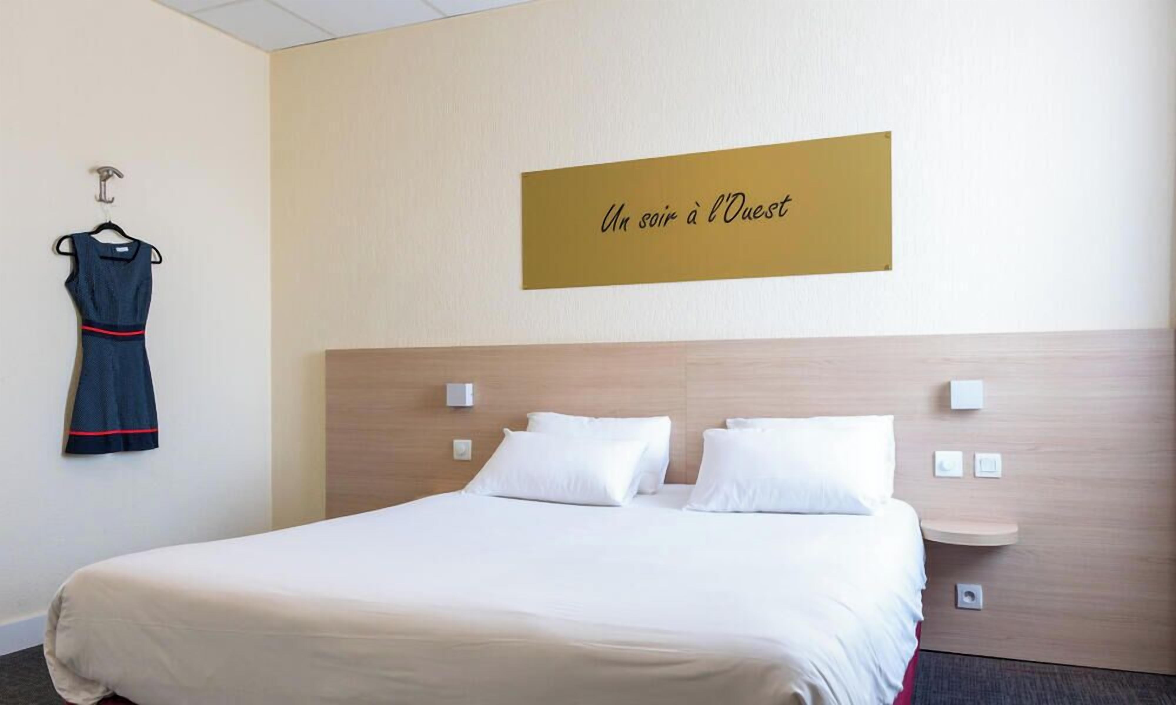 A hotel room with a bed, a wall-mounted sign, a coat rack, and a small bedside table.