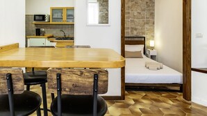 A compact room with a bed, a small kitchenette, and a dining area with chairs.