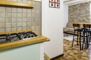 A kitchen with a gas stove, a wooden countertop, a tiled backsplash, a stone wall, a sofa, and a dining area with stools. - GuestHost Comfy APT in the historic center (Alghero)