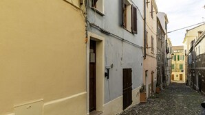 A narrow cobblestone street flanked by buildings with doors and windows, suggesting a historic or residential area.