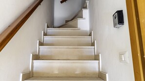 A staircase with white steps and a wooden handrail, leading to a landing with a light switch and a wall-mounted device.
