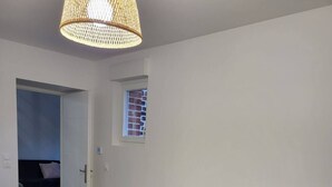 Ein modernes Schlafzimmer mit einem großen Bett, einem kleinen Fenster und einer gewebten Leuchte.