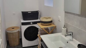 Ein kleines Badezimmer mit Waschmaschine, Waschbecken und Spiegel.