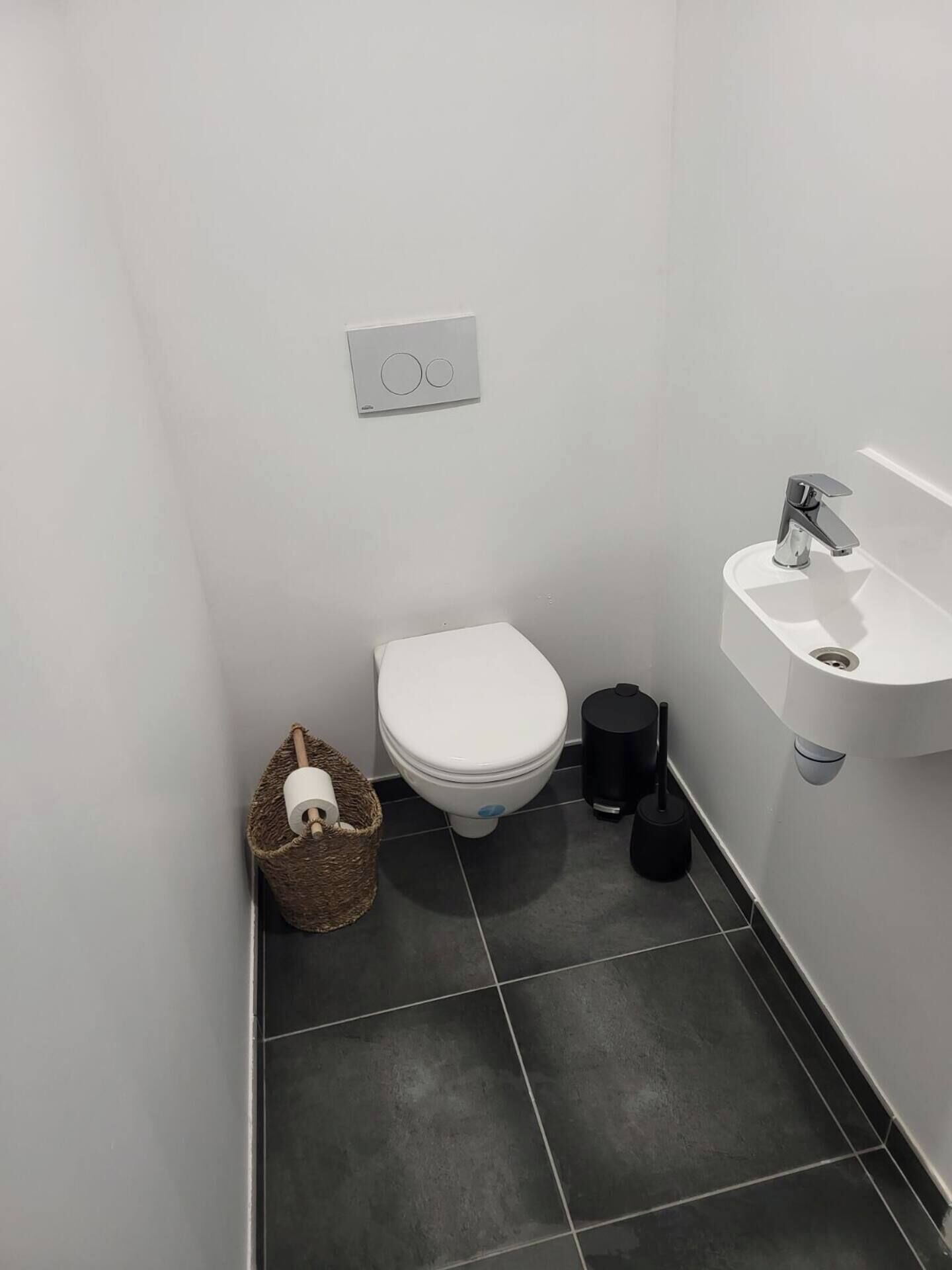 Een kleine, moderne badkamer met een wit toilet, een zwarte prullenbak en een witte wasbak.