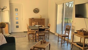 Ein geräumiges Wohnzimmer mit einem grünen Sofa, einem Essbereich mit Holztisch und -stühlen, einem großen Fenster und einem Fernseher.