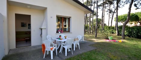 A modern house with a patio, white chairs, and a small table.