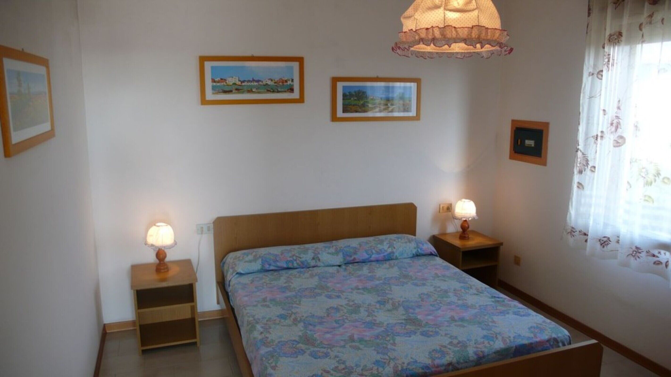 A bedroom with a wooden bed, two bedside tables with lamps, and two framed pictures on the wall.