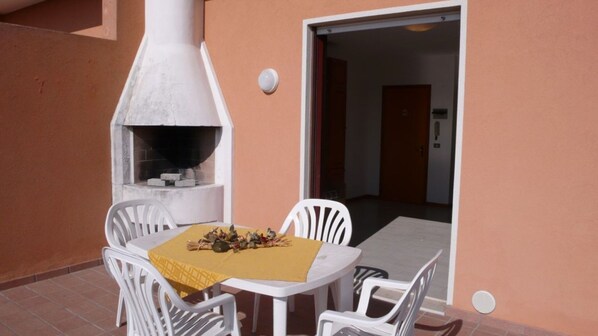 An outdoor patio with a white table and chairs, a pizza oven, and a yellow tablecloth.