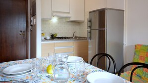 A kitchen with a dining table set for two, a refrigerator, and a stove. - Spacious flat with a solarium (Bibione)