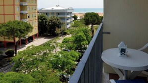 Un balcon donnant sur une plage, un immeuble à la façade rouge et jaune, et une table blanche agrémentée d’un petit objet décoratif.