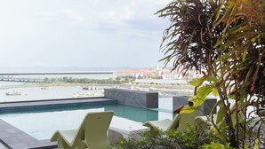 A pool area with modern chairs and a view of the sea and buildings. - 1 bdr apartment with Ocean View and Social area w/ pool (Avenida Balboa)