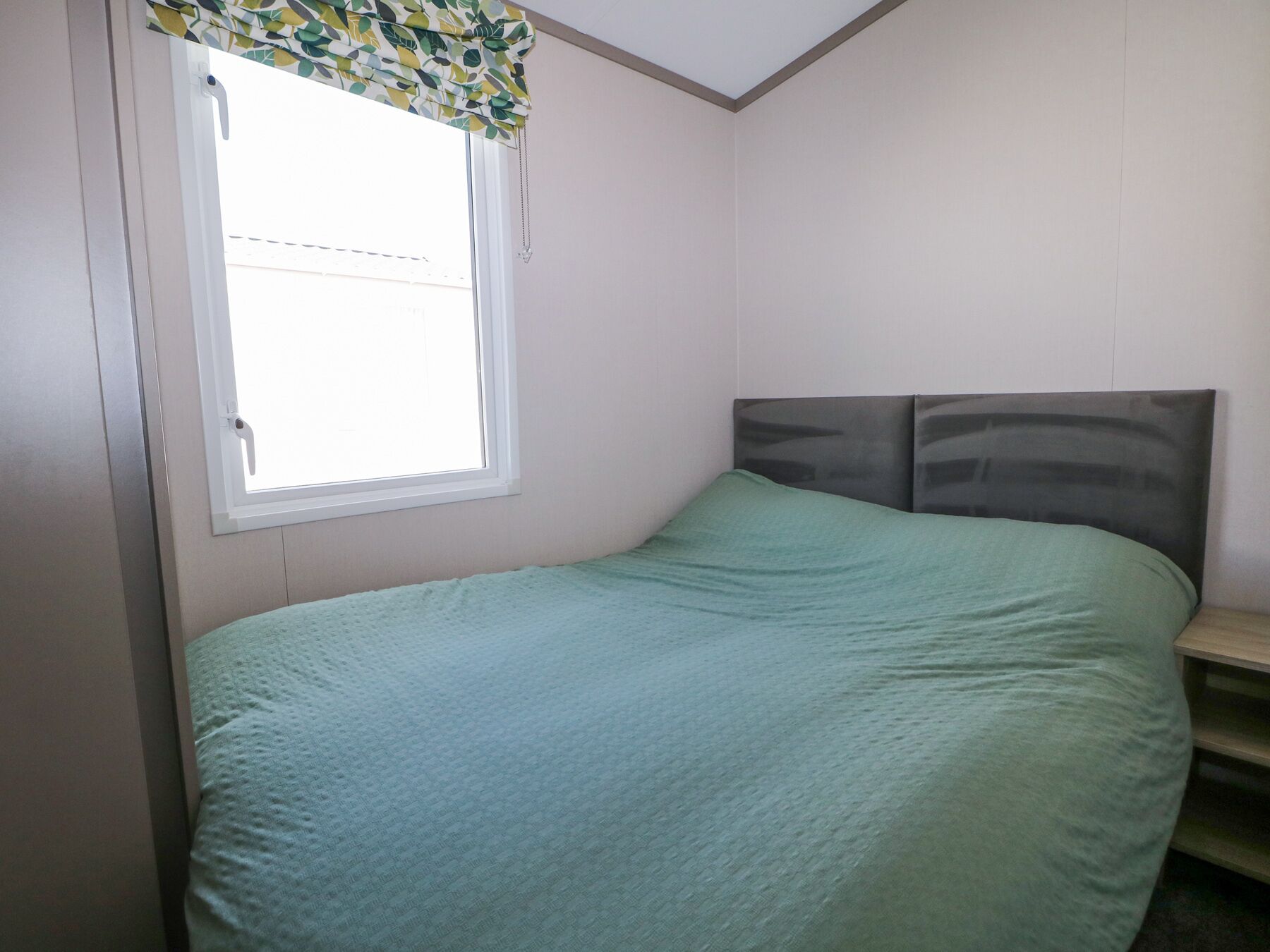 Una camera da letto con un letto singolo, una finestra con tenda a motivi fogliari e una testiera semplice.