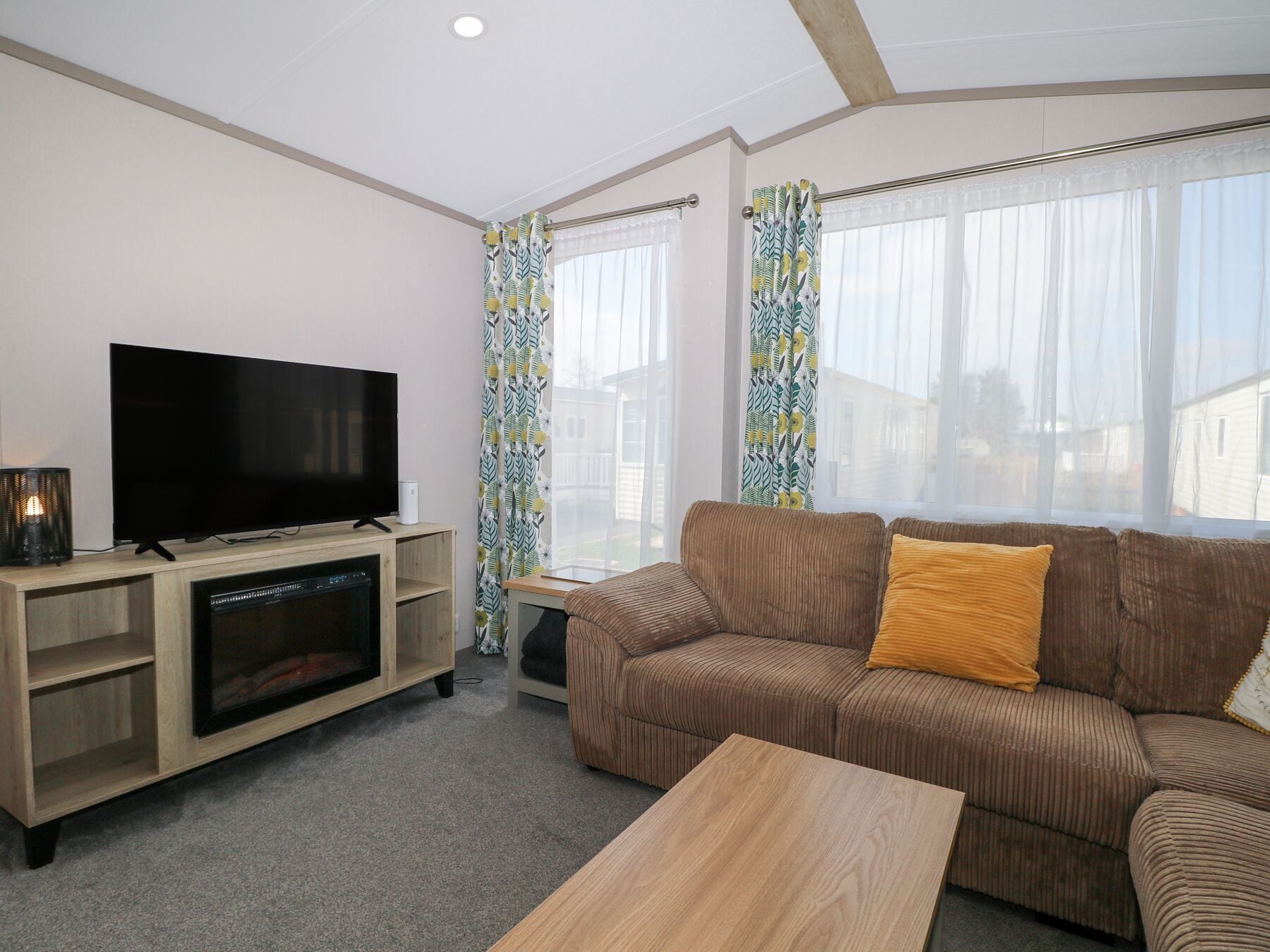 A living room with a flat-screen TV, wooden entertainment unit, brown sofa, and a wooden coffee table.