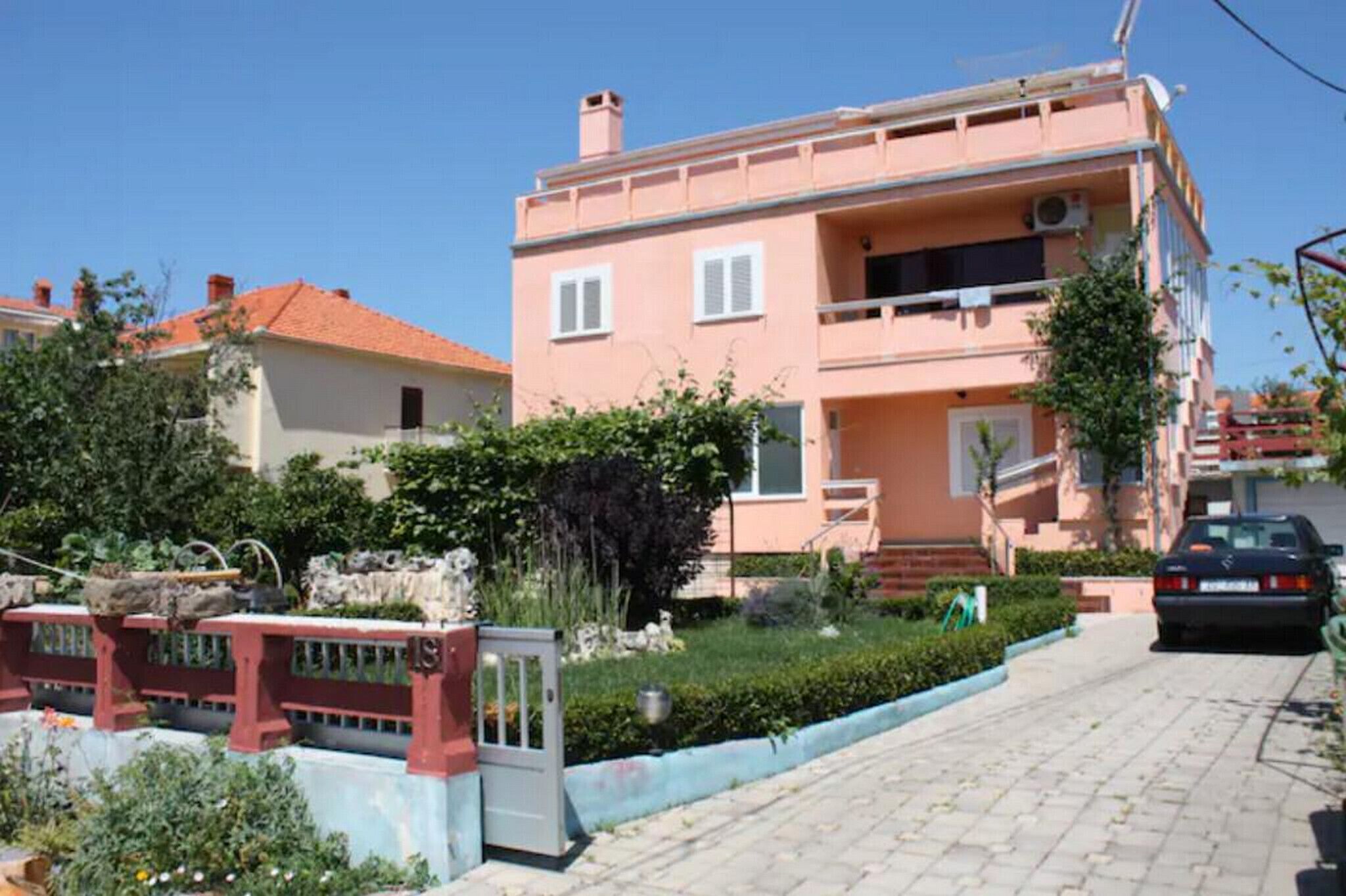 A two-story residential building with a red-tiled roof, a balcony on the second floor, and a paved driveway.