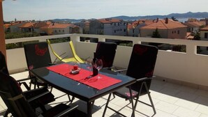Een terras met een gedekte tafel voor twee, met uitzicht op een woongebied met rode pannendaken.