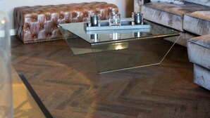 A modern living room with a glass coffee table, a brown leather ottoman, a grey sofa, and a vase with tall grasses. - Langschläfer - New: Apartment Langschläfer 4th floor, best location on the beach (Westerland)
