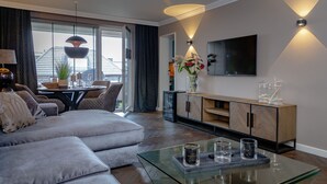 A modern living room with a sectional sofa, a glass coffee table, a wooden cabinet, and a flat-screen TV mounted on the wall. - Langschläfer - New: Apartment Langschläfer 4th floor, best location on the beach (Westerland)