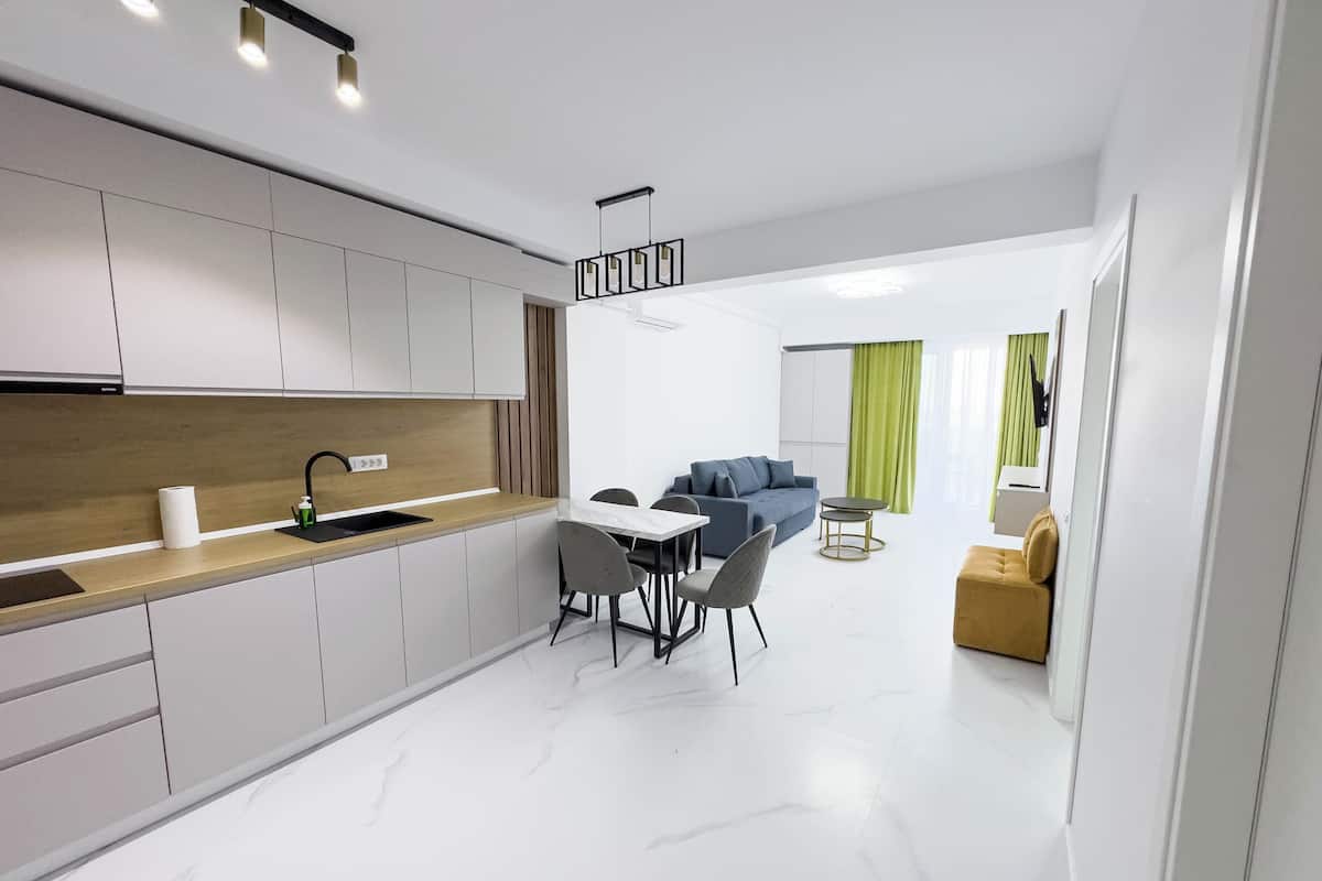 Una cocina moderna con armarios blancos, encimera de madera y grifo negro. Hay una zona de comedor con mesa y sillas, y un sofá azul al fondo.
